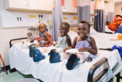 Three little orthopedic patients laugh and play on one of the ward beds.